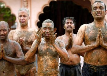 Men pray after applying cow dung on their bodies in the belief that it will boost their immunity against Covid-19 at the Shree Swaminarayan Gurukul Vishwavidya Pratishthanam Gaushala on the outskirts of Ahmedabad in May 2021. | Reuters