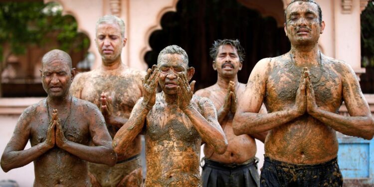 Men pray after applying cow dung on their bodies in the belief that it will boost their immunity against Covid-19 at the Shree Swaminarayan Gurukul Vishwavidya Pratishthanam Gaushala on the outskirts of Ahmedabad in May 2021. | Reuters